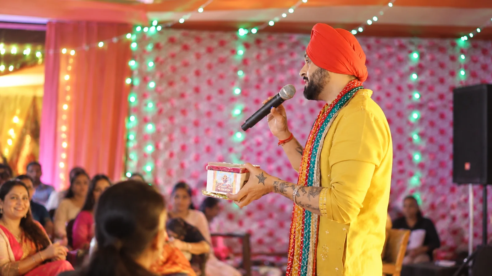 Turbaned performer interacting with audience under warm festive ambient lights